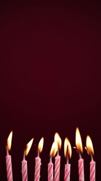 Row of colorful burning birthday candles on red background. Bright flames and vibrant colors with space for text or graphic elements. Ideal for birthday celebration concepts.