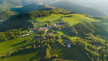 Obraz premium Aerial view of small rural village among green hills forests and fields during golden sunset light in German countryside