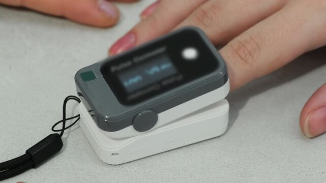 Modern pulse oximeter measures heartbeat on woman finger in clinic closeup. Female patient undergoes heart checkup in hospital slow motion