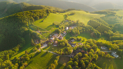 Aerial sunset view of small rural village surrounded by green hills forests and farmland in German countryside © StockMediaSeller