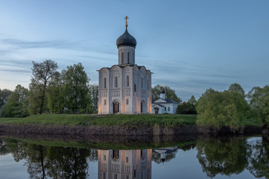 Historic Church of the Intercession on the Nerl reflected in calm river water at sunset, famous white stone Orthodox church near Vladimir and Suzdal, Russia, scenic spring landscape with dramatic sky.