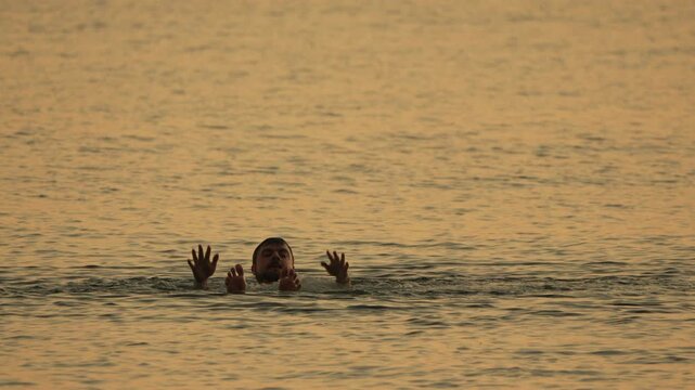 Man floating water, man's head visible, hands and feet emerge from golden hour ocean.