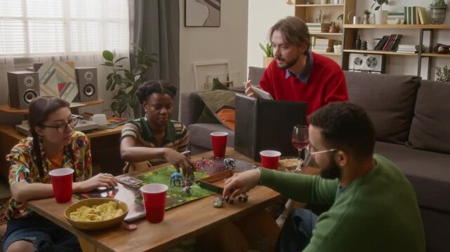 High angle shot of group of friends playing tabletop role-playing game, game master running scenario from behind screen, while players taking turns around the table in cozy living room
