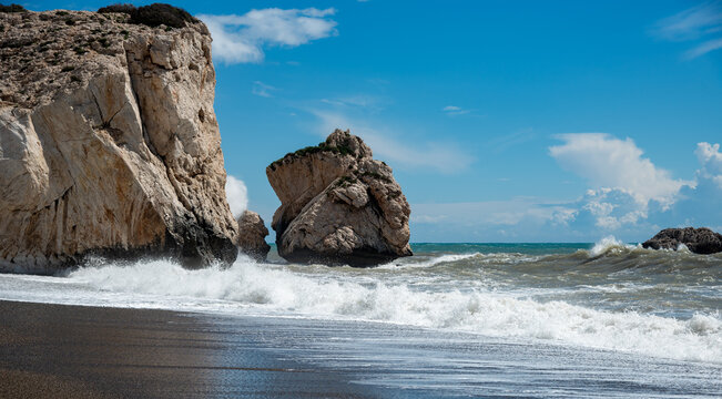Iconic large rock formation known as aphrodite's rock on a dark pebble beach with powerful ocean waves breaking against the coast. Paphos Cyprus