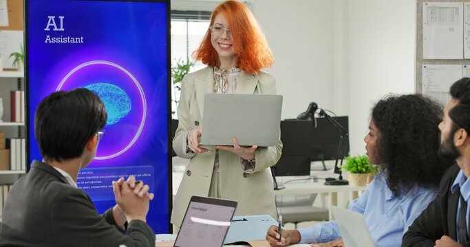 Woman software engineer or tech entrepreneur holding a laptop presenting an AI assistant application on a large display screen. Digital automation and machine learning solutions during a business.