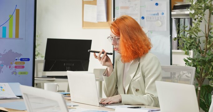 Businesswoman or programmer working on a computer while looking at AI assistant interface on monitor at office. Smart workplace automation, future software engineering, machine learning concept.