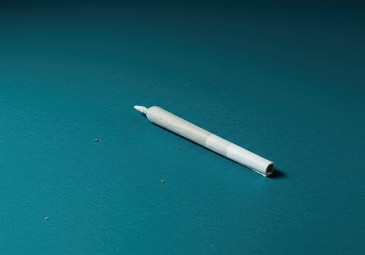 A single cannabis preroll joint resting on a vibrant, deep teal background, highlighting its preparation and ready-to-use form, cylindrical, aqua, background