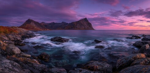 Obraz premium A coastal scene features mountains, ocean, and a striking sunset with a vibrant sky and rocky shore