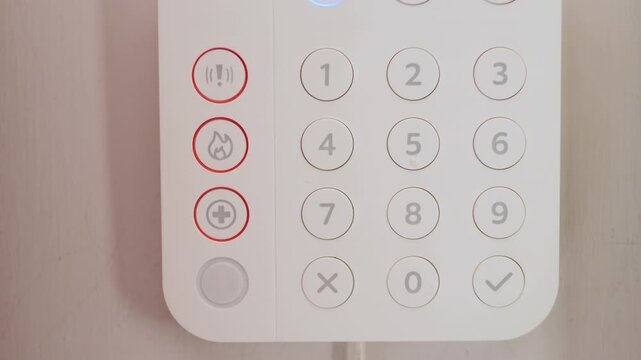 Female fingers type a numeric security code on a home alarm keypad while activating the domestic security system indoors at home.