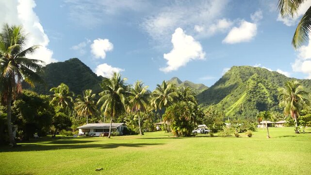 Tropical valley volcanic mountains palm trees framing sunlit bungalow manicured lawn towering green ridges rise behind coconut palms under azure sky serene atmosphere island Tahiti, French Polynesia