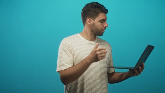 Hispanic man with beard holding laptop and gesturing with his hand in studio; focus productivity remote work.
