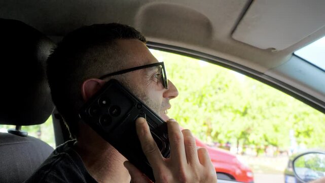 A smiling young man casually talks on his phone while driving, dangerously distracted from the road, unaware that his reckless behavior puts himself and others at serious risk