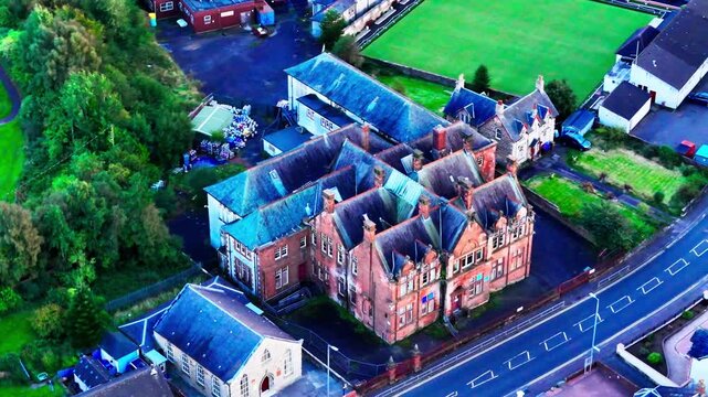 Cinematic drone tracking shot of the historic derelict old primary school building in Dreghorn, Ayrshire, showcasing abandoned red brick architecture