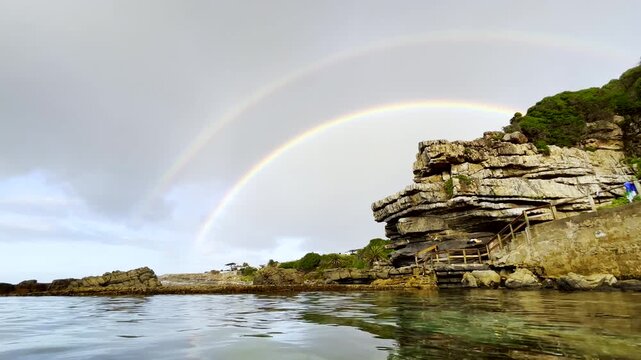 Pretty double rainbow viewed from over calm ocean marine pool on coastline