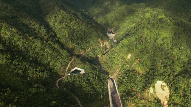 Aerial flyover of a small mountain water dam near Obi, Caramoran, surrounded by lush tropical hills and rural terrain - Philippines
