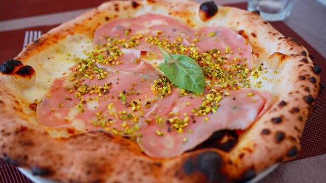 Wood-fired Neapolitan pizza from Pompei with mortadella, crushed pistachios, basil, creamy cheese, and a blistered crust on a restaurant table.
