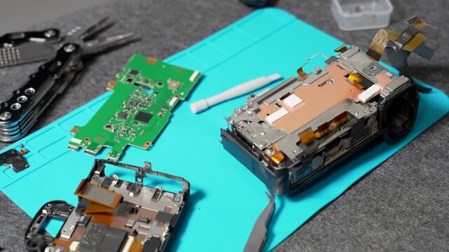 Camera components and circuit boards laid out on a workbench during electronic repair, showing intricate internal technology.