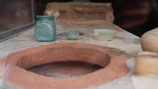 Small ancient vessels displayed on a Pompeii thermopolium counter, with a circular dolium opening, glass jar, bowl, and preserved Roman food shop surface.