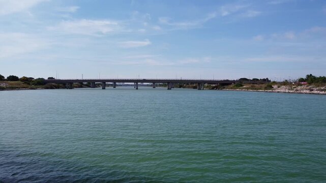 4K fast drone video flying under a highway bridge over the Turia River mouth in Valencia, Spain. The shot reveals multiple bridges ahead and birds flying over the water on a sunny day