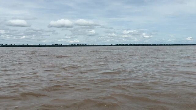 A vast expanse of muddy river water stretches under a cloudy sky in the Amazon Basin. Ideal for environmental documentaries or educational content.