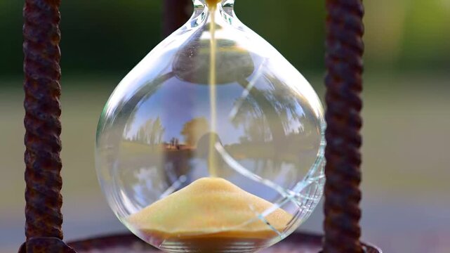 Close up of an hourglass with sand flowing through the neck.