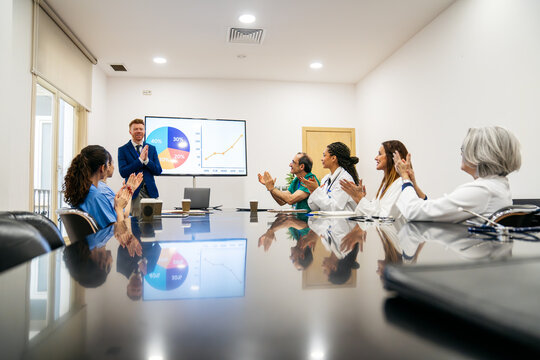 Medical professionals including doctors and nurses applauding a business leader after a successful presentation in a modern conference room