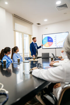 Diverse medical team including doctors and nurses attending a presentation on clinic data and healthcare statistics in a modern hospital boardroom
