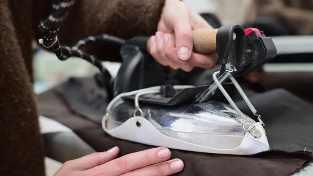 Close up of a tailor using a professional steam iron on black fabric in a fashion workshop