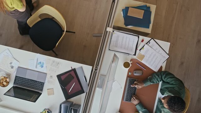 Overhead shot of business team reviewing statistics and planning strategy while working at separate office desks with digital devices and paperwork