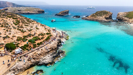 Landscape aerial drone shot of the blue lagoon beach and port in malta, comino island with green foliage and limestone rock and sandy beach busy with tourists in summer © STJMEDIA