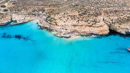 Landscape aerial drone shot of the blue lagoon beach and port in malta, comino island with green foliage and limestone rock and sandy beach busy with tourists in summer © STJMEDIA