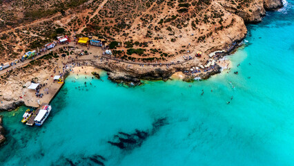 Landscape aerial drone shot of the blue lagoon beach and port in malta, comino island with green foliage and limestone rock and sandy beach busy with tourists in summer © STJMEDIA