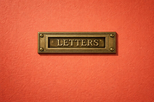 Letterbox plate made of antique brass with embossed letters mounted on an orange wall for vintage house entrance decor.