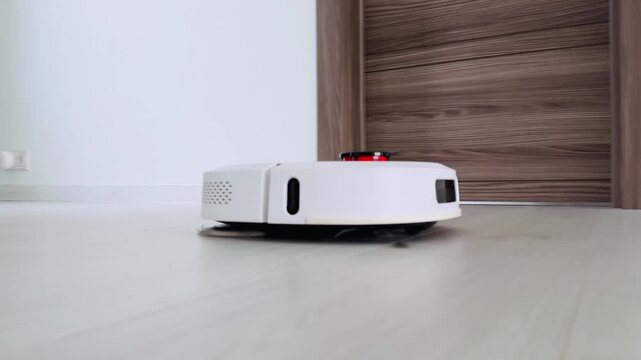 Robot vacuum cleaner navigating smooth wooden floor beneath green wall and doorway