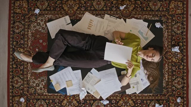 Top view of tired office employee lying on desk surrounded by paperwork and reports, illustrating stress, burnout and workload pressure