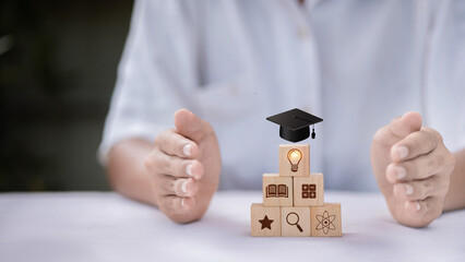 Hands Protecting Pyramid of Wooden Cubes with Education Icons — Graduation Cap, Lightbulb, Book, Science, and Knowledge Building Concept © จุฑารัตน์ เจริญวงษ์