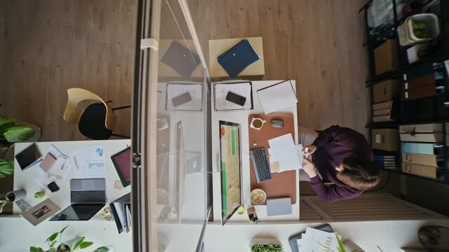 Overhead shot of stressed office employee sitting at cluttered desk with paperwork and desktop computer while writing word help with red marker
