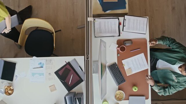 Overhead office scene with young professionals sitting at separate desks with laptop and desktop computer and starting paperwork tasks