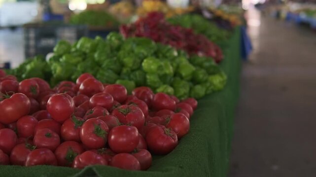 Ripe tomatoes and green peppers closeup market stall, rich textures and vibrant color contrast, soft bokeh aisle depth, vendor arranging display, shoppers