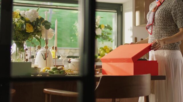Woman opening red gift box at festive dining table with flowers