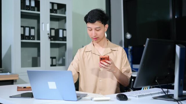 Young Asian businessman using a smartphone app for digital verification while working on a laptop late
