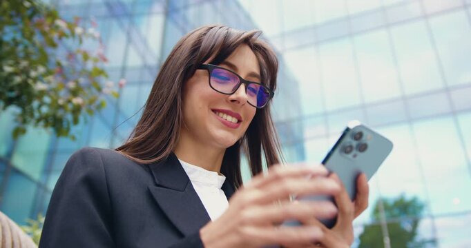 Young woman outdoors using a smartphone app, texting, gaming, shopping online, and ordering delivery while smiling and sharing content on social media.