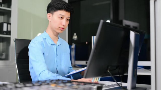 Young Asian businessman using a smartphone app for digital verification while working on a laptop late