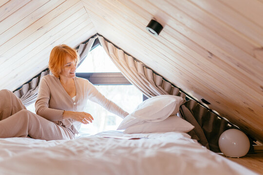 Smiling Mature Woman Making Bed In Cozy Loft Bedroom