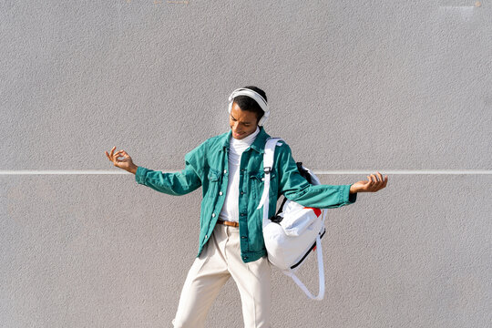 Man wearing headphones listening music while dancing against gray wall
