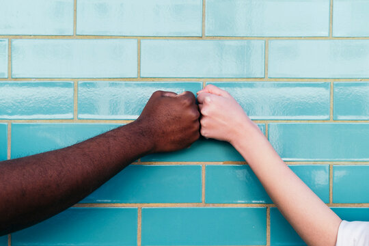 Multiracial friends giving fist bump on turquoise brick wall