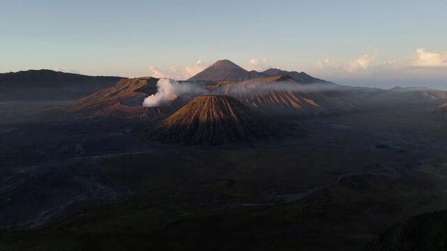 Cinematic drone shot flying slowly forward over the vast volcanic valley of Mount Bromo and Mount Batok. Majestic mountain landscape in East Java, Indonesia, during a soft morning sunrise.
