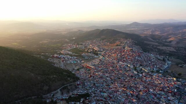 Cinematic drone aerial view of a Moroccan mountain city at sunset with dense urban buildings, surrounding hills, and warm golden light. Ideal for travel and documentary projects.