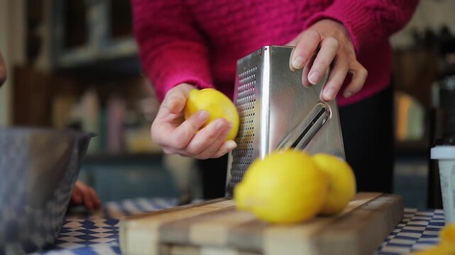 woman shreds lemon peel with grater on kitchen table for citrus zest