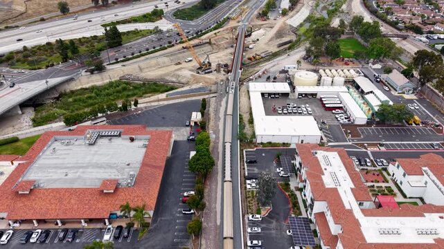 Cinematic Aerial view of a train departing San Juan Capistrano heading toward San Diego. The shot uses a 4k camera drone to capture a downward view from behind.